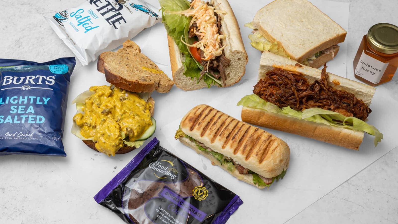 Sandwiches, a French stick, a panini, crisps and a jar of honey